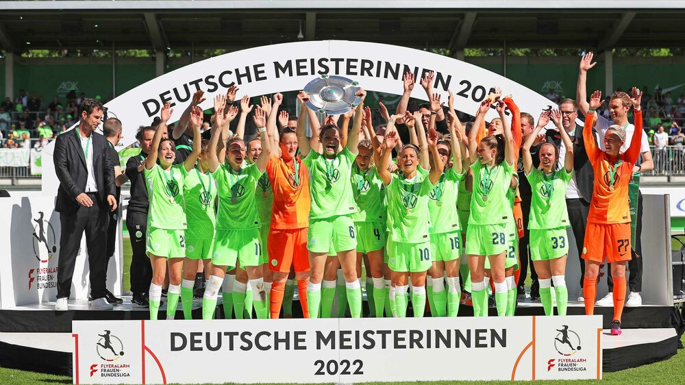 Die Spielerinnen des VfL Wolfsburg feiern mit erhobenen Händen und der Meisterschale.