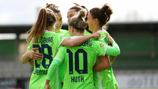 Huth, Waßmuth und weitere Frauen des VfL Wolfsburg liegen sich auf dem Platz im AOK Stadion jubelnd in den Armen.