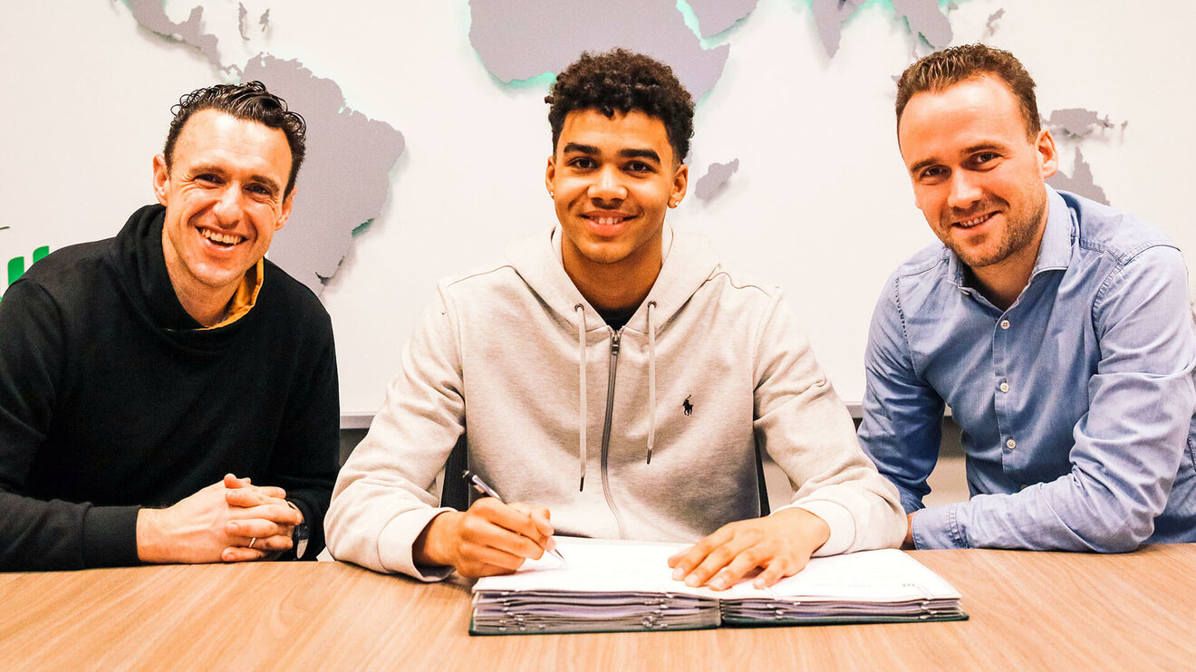 VfL Wolfsburg Spieler Odogu posiert mit Stift in der Hand bei deiner Vertragsunterzeichnung.