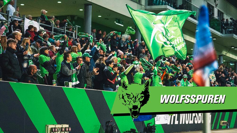 Die Fans des VfL-Wolfsburg jubeln zusammen. Auf der rechten Bildseite ist das Logo der Wolfsspuren zu sehen.