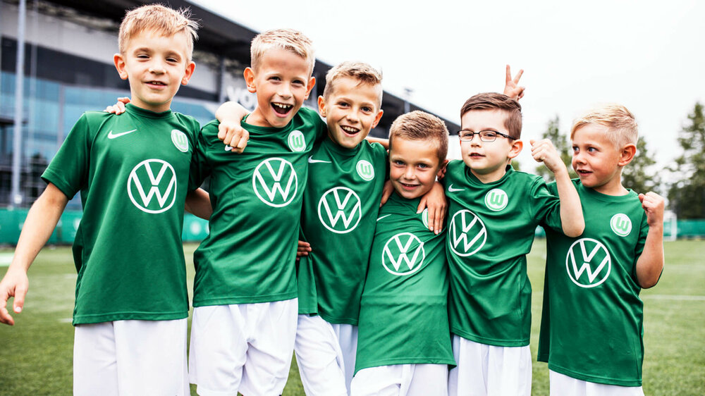 Lachende Kinder der VfL-Fußballschule Arm in Arm vor der Volkswagen Arena. 