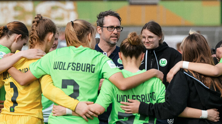 Die Spielerinnen der VfL Wolfsburg U17 steht im Kreis auf dem Platz, ihre Arme um die Schultern der Nebenfrauen gelegt.
