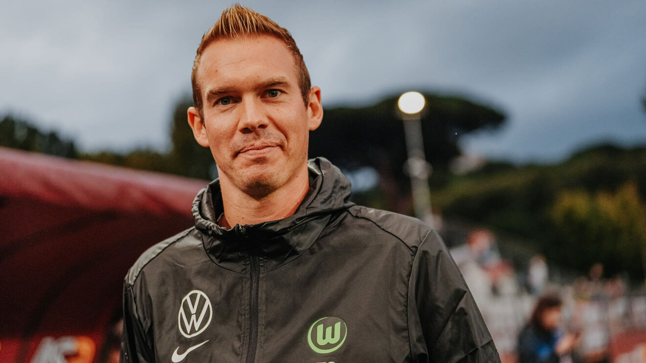 Der VfL-Wolfsburg-Trainer Tommy Stroot läuft lächelnd neben dem Spielfeld.