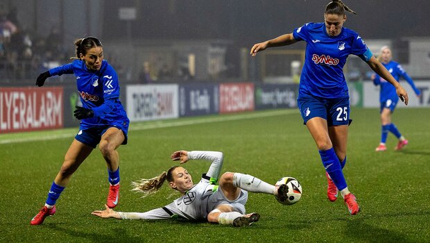 Sarai Linder vom VfL-Wolfsburg liegt mit der linken Seite auf dem Boden. Mit dem rechten Fuß spielt sie noch den Ball. Rechts und Links neben ihr zwei Gegenspielerinnen die versuchen an den Ball zu kommen. 