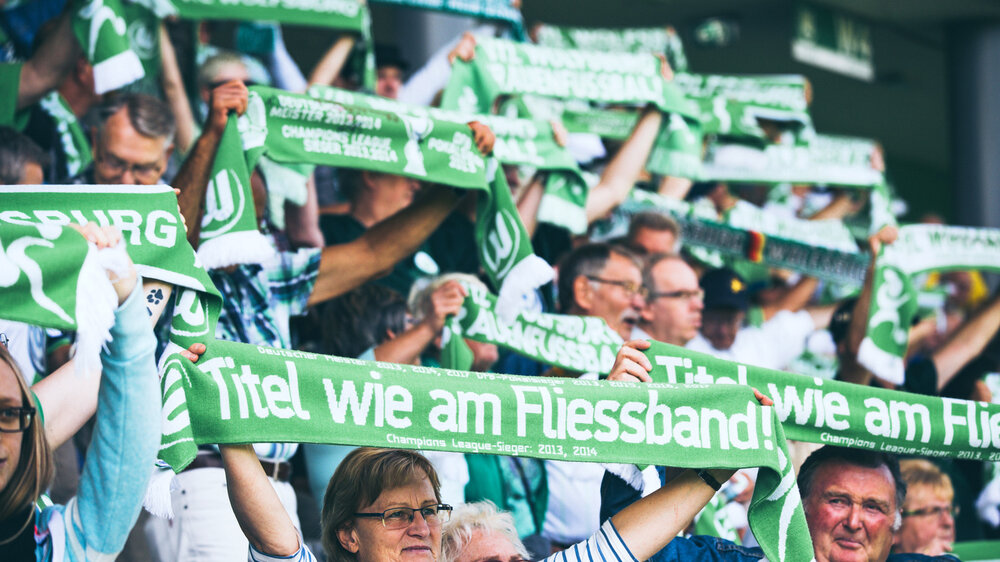 Die Fans des VfL Wolfsburg halten im AOK Stadion in Wolfsburg die Schals in die Luft.
