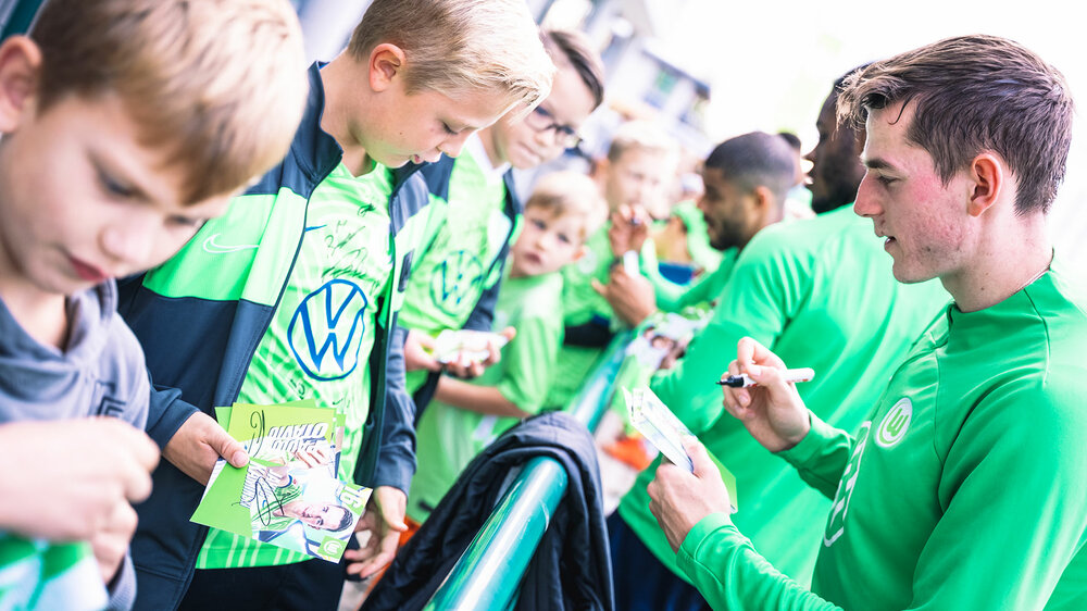 Spieler des VfL Wolfsburg geben Fans Unterschriften und Autogramme.