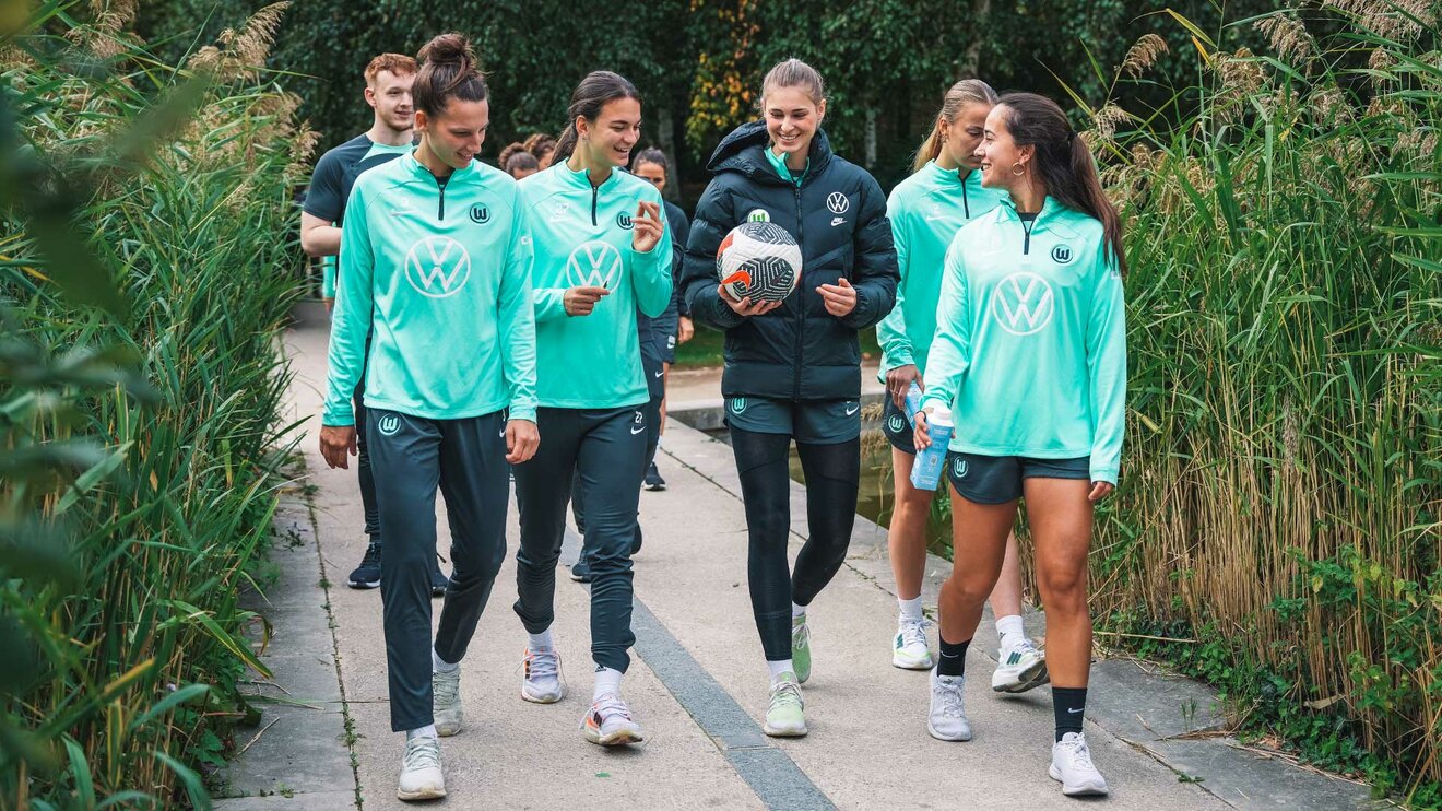 VfL-Wolfsburg-Spielerin Riola Xhemaili spaziert mit drei Mitspielerinnen und lacht.
