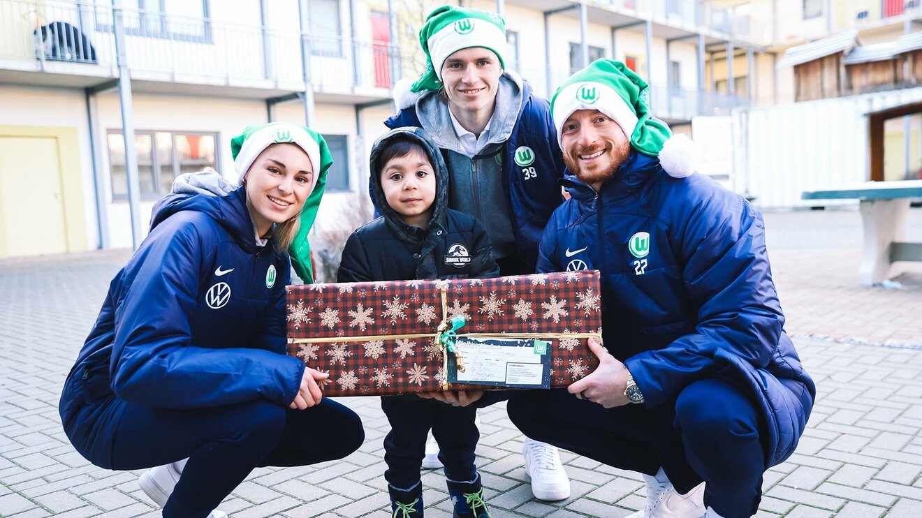 Die VfL-Wolfsburg-Akteure Jule Brand, Patrick Wimmer und Maximilian Arnold übergeben einem Jungen ein Geschenk.
