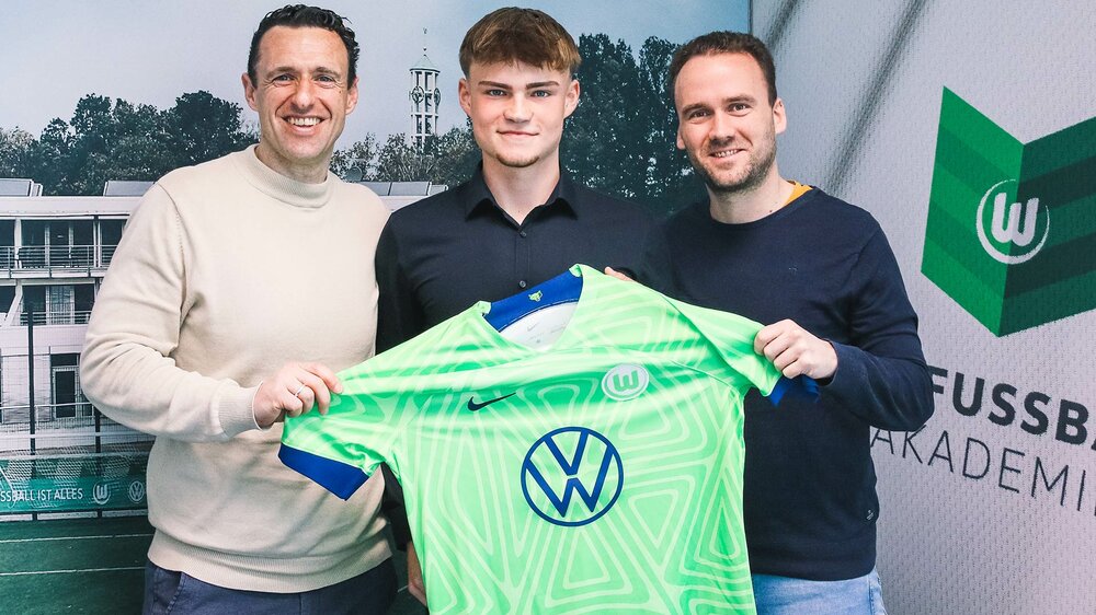 Akademie-Direktor Michael Gentner, Manuel Braun und eine weitere Person halten ein Trikot des VfL Wolfsburg hoch.