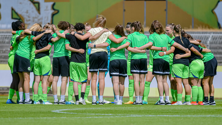 Die VfL-Wolfsburg-Spielerinnen der U20 Mannschaft der Frauen versammeln sich in einem Kreis auf dem Rasen.