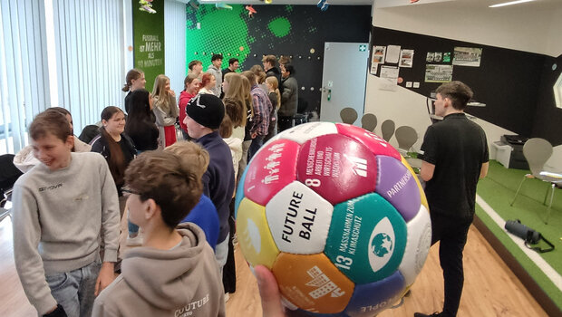 Ein Handball mit einer Gruppe von Kindern im grün-weißen Klassenzimmer des VfL Wolfsburg