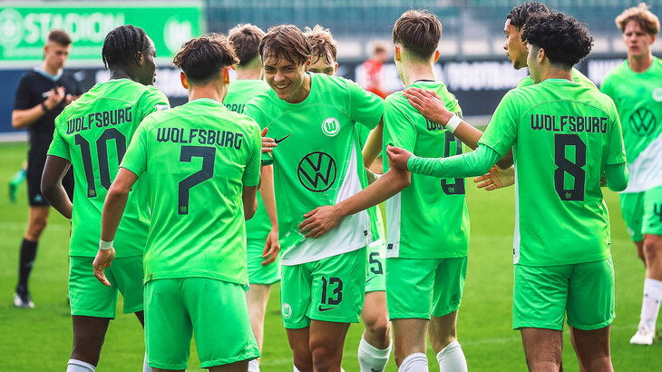 Die Spieler der U19 Mannschaft des VfL Wolfsburg stehen zusammen auf dem Feld und ein Spieler lächelt in die Kamera. Die Stimmung scheint positiv.