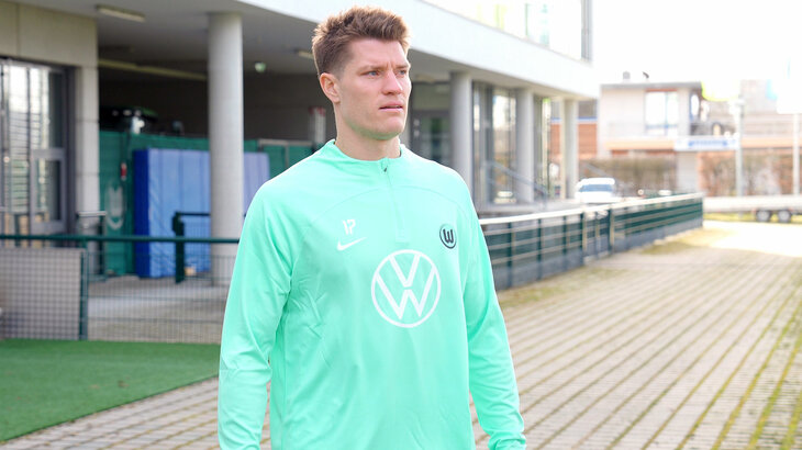 VfL-Wolfsburg-Neuzugang Kevin Behrens geht lächelnd an der Kamera vorbei in Richtung des Trainingsplatzes.