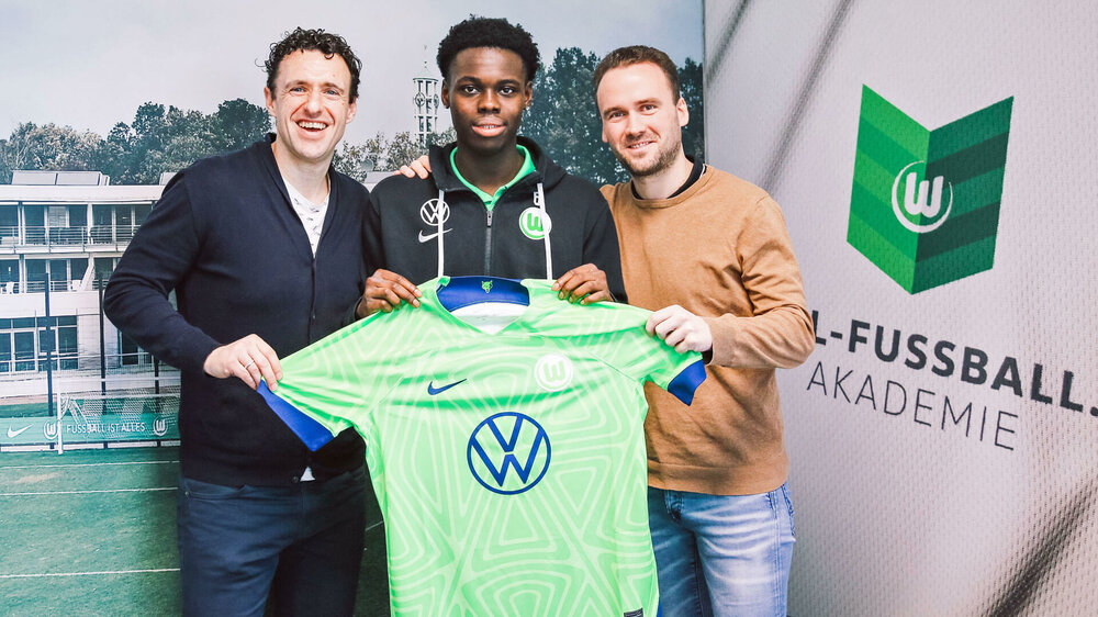 Der VfL-Wolfsburg-Spieler Kofi Amoako hält mit den Verantwortlichen ein Trikot hoch.