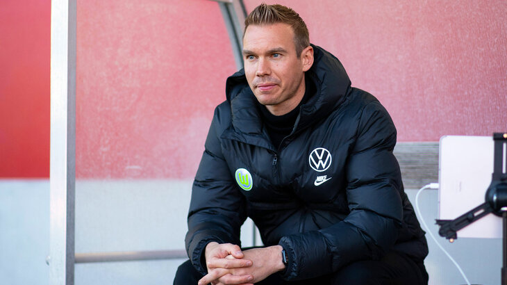 VfL-Wolfsburg-Trainer Tommy Stroot sitzt auf der Trainerbank.