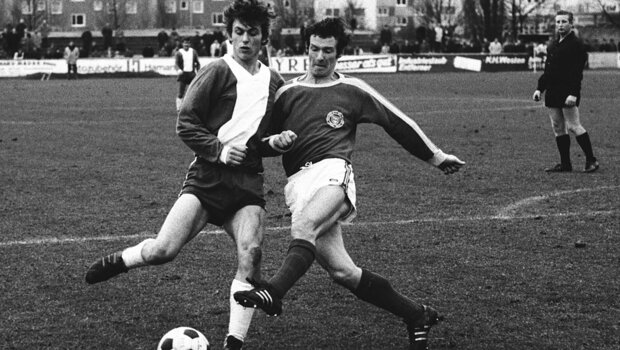 Ein schwarz-weiß Bild aus einem historischen Spiel des VfL gegen Kiel, wobei zwei Spieler im Zweikampf um den Ball gegeneinander sind.