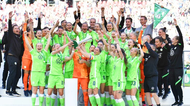 VfL-Wolfsburg-Spielerinnen stemmen den DFB-Pokal auf dem Siegerpodest zusammen in die Höhe.