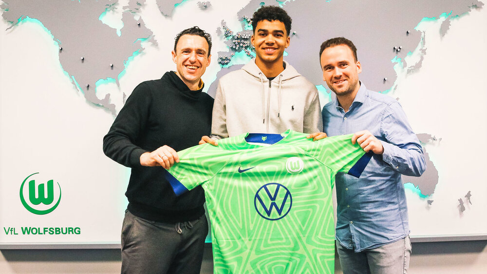 VfL Wolfsburg Spieler Odogu posiert nach seiner Vertragsunterzeichnung mit den Funktionären und einem Trikot.
