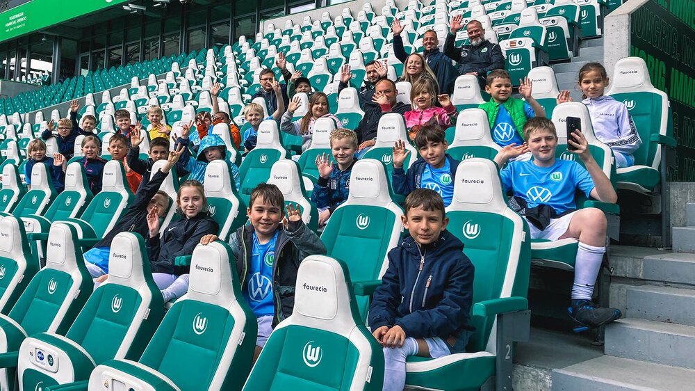 Kinder sitzen in VfL-Wolfsburg-Trikots auf der VIP-Tribüne in der Volkswagen Arena.
