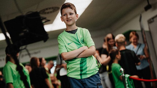 Ein Junge posiert im neuen Heimtrikot des VfL Wolfsburg und verschränkt die Arme vor der Brust..