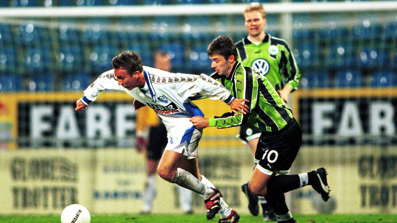 Ein historisches Bild von einem Zweikampf zwischen einem Spieler von Bochum und einem VfL-Wolfsburg-Spieler.