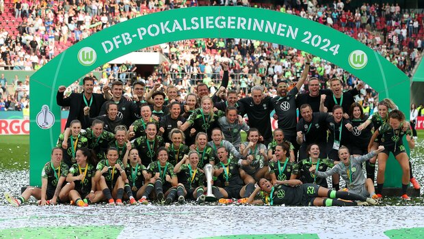 Mannschaftsfoto der VfL-Frauen vor dem Banner "DFB-Pokalsiegerinnen 2024". Die Spielerinnen jubeln und einige strecken ihre Arme vor Freude in die Luft. 
