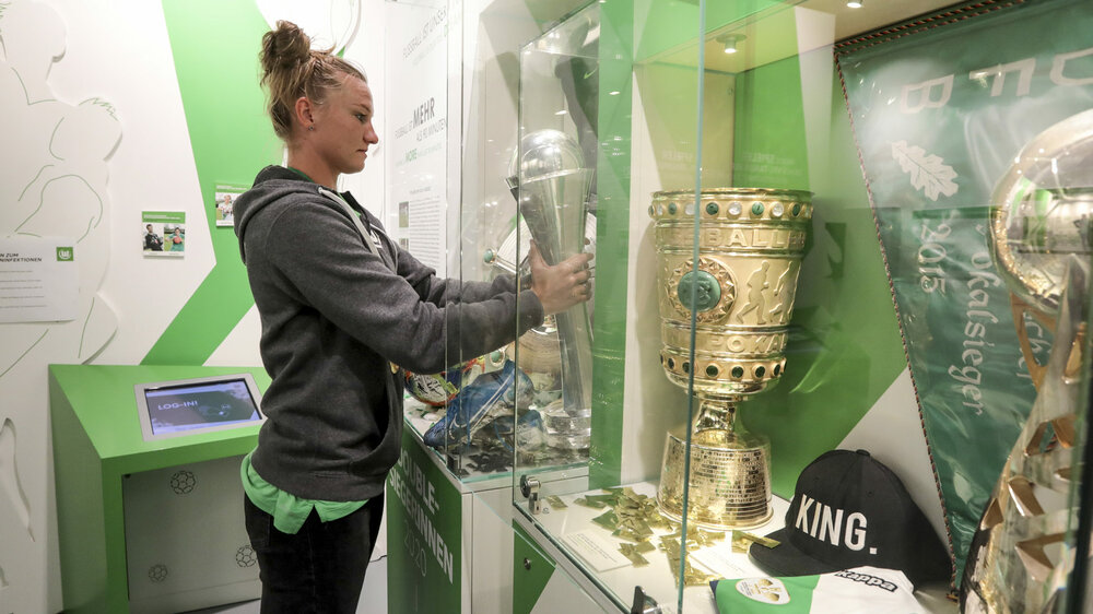 Alexandra Popp nimmt den DFB Pokal aus einer Vitrine.