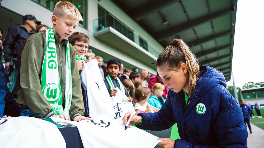 VfL-Wolfsburg-Spielerin Jule Brand unterschreibt auf dem Trikot eines Jungen.