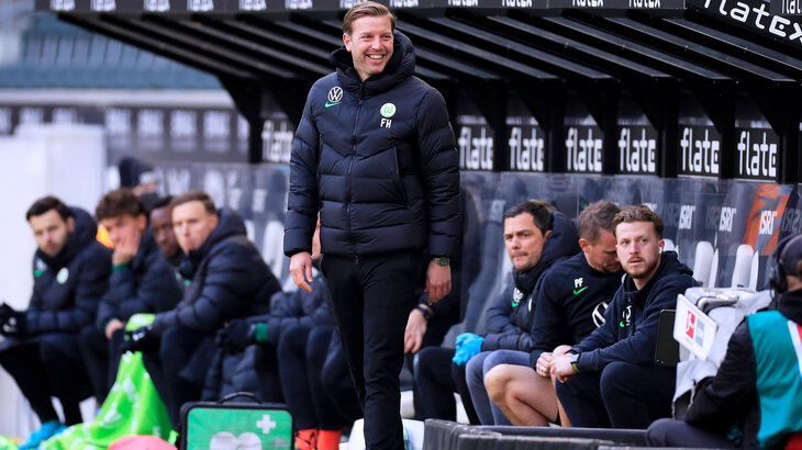 VfL Wolfsburg-Trainer Kohfeldt lacht vor der Ersatzbank.