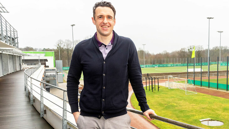 Michael Gentner, Direktor des VfL Wolfsburg-Akademie lehnt an einem Gelände. Im Hintergrund sieht man die Fußballplätze der Akademie.