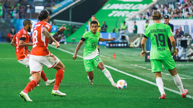 VfL Wolfsburg Spieler Rogerio hat auf dem Spielfeld den Ball am Fuß und wird von einem Gegenspieler von Union Berlin angegriffen.