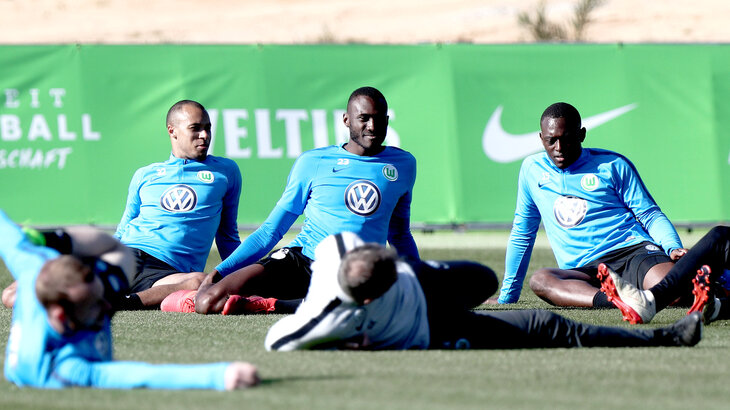 Drei Spieler des VfL Wolfsburg beim Dehnen auf dem Trainingsplatz.