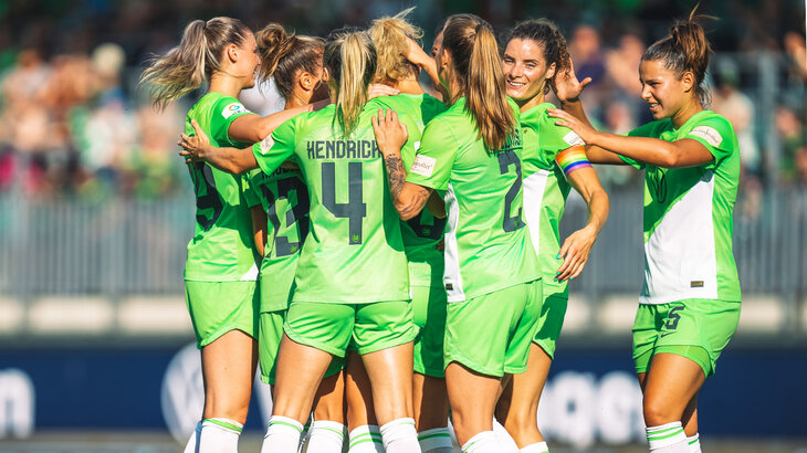 Spielerinnen des VfL Wolfsburg stehen in einer Gruppe zusammen und jubeln.