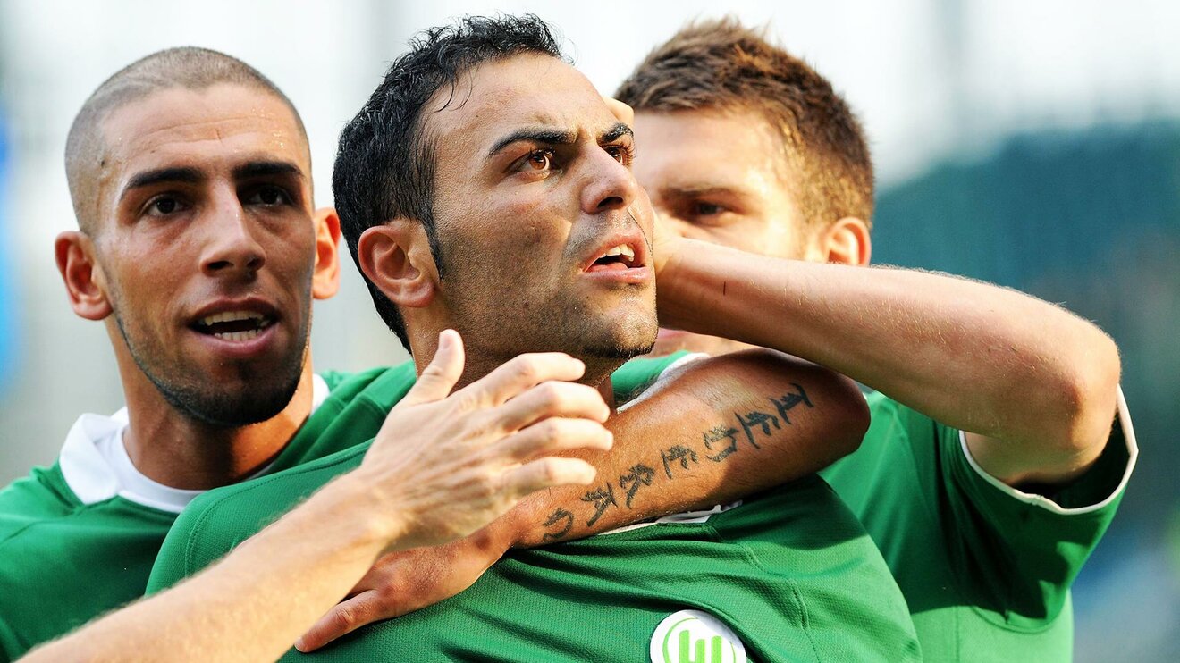 Der ehemalige Spieler des VfL Wolfsburg Mahir Saglik wird von seinen Mitspielern umarmt und schaut dabei nach oben.