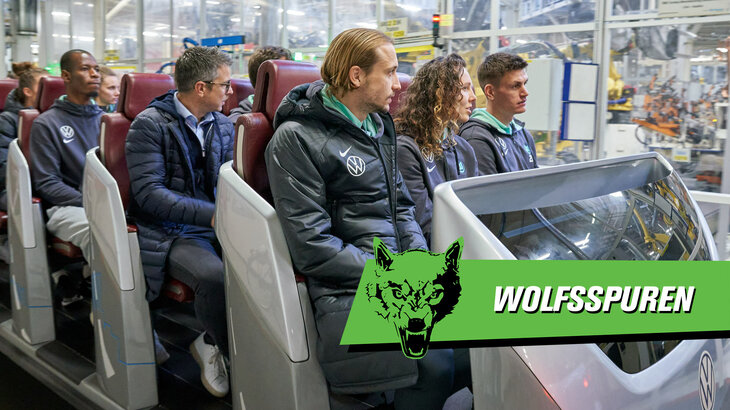 Eine VfL Wolfsburg Grafik mit der Aufschrift "Wolfsspuren" liegt auf einem Foto von Lovro Majer, Fenna Kalma und Joakim Maele, welche in einem Zugfahrzeug sitzen.