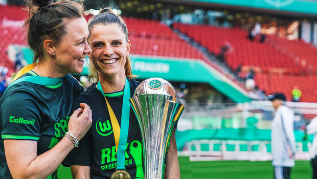 Tabea Sellner hält einen Pokal in der Hand, lächelt in die Kamera und wird von Marina Hegering umarmt.