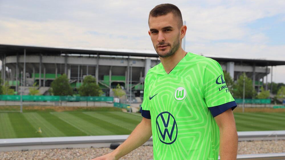 Bartol Franjic posiert im Trikot des VfL Wolfsburg vor dem Trainingsgelände.