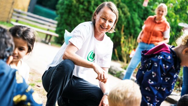 Die ehemalige VfL-Wolfsburg-Spielerin Conny Pohlers hockt lachend bei Kindern.