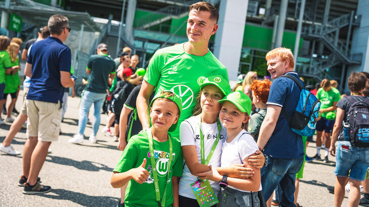 Ein Spieler des VfL Wolfsburg posiert vor der Volkswagen Arena mit kleinen VfL-Fans.