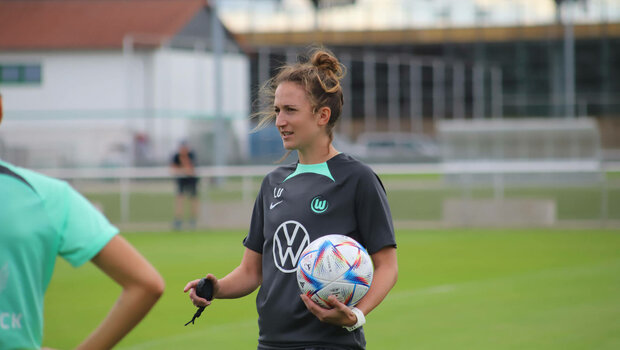 Die VfL-Wolfsburg-Spielerin Trainerin Laura Vetterlein hält einen Ball im Arm.