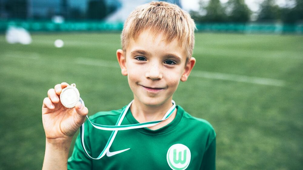 Ein Kind der VfL Wolfsburg-Fußballschule hält lächelnd eine Medaille in die Kamera.