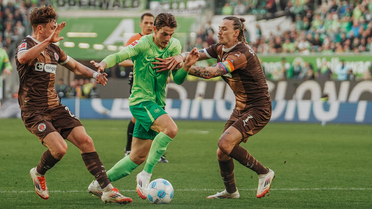 VfL-Wolfsburg-Spieler Jakub Kaminski befindet sich im Zweikampf mit zwei gegnerischen Spielern des FC. St. Pauli.