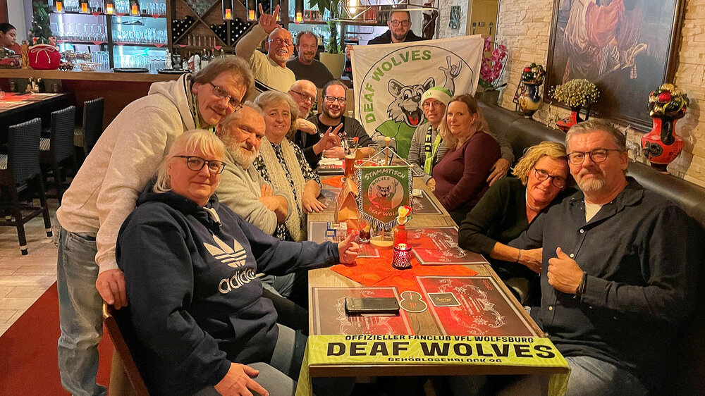 Ein Gruppenbild vom VfL Wolfsburg-Fanclub Deaf Wolves an einem Tisch.