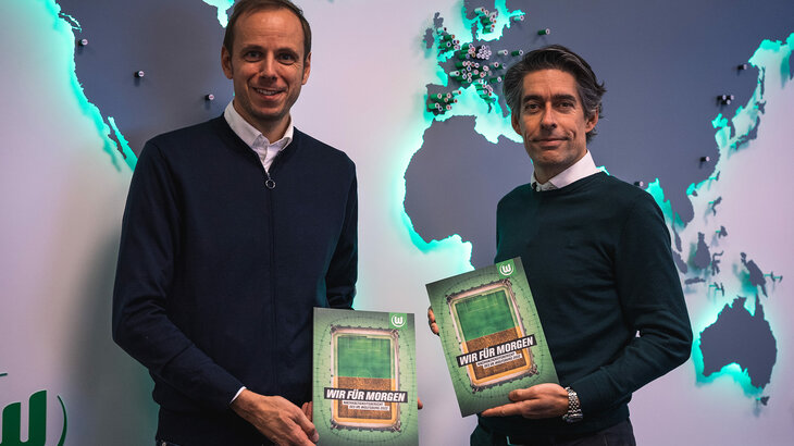 Nico Briskorn und VfL-Wolfsburg-Geschäftsführer halten den Nachhaltigkeitsbericht 2022 in den Händen.