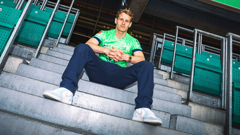 Der neue VfL-Wolfsburg-Spieler Nicolas Cozza sitzt auf der Fantribüne. Dabei trägt er sein neues Trikot.
