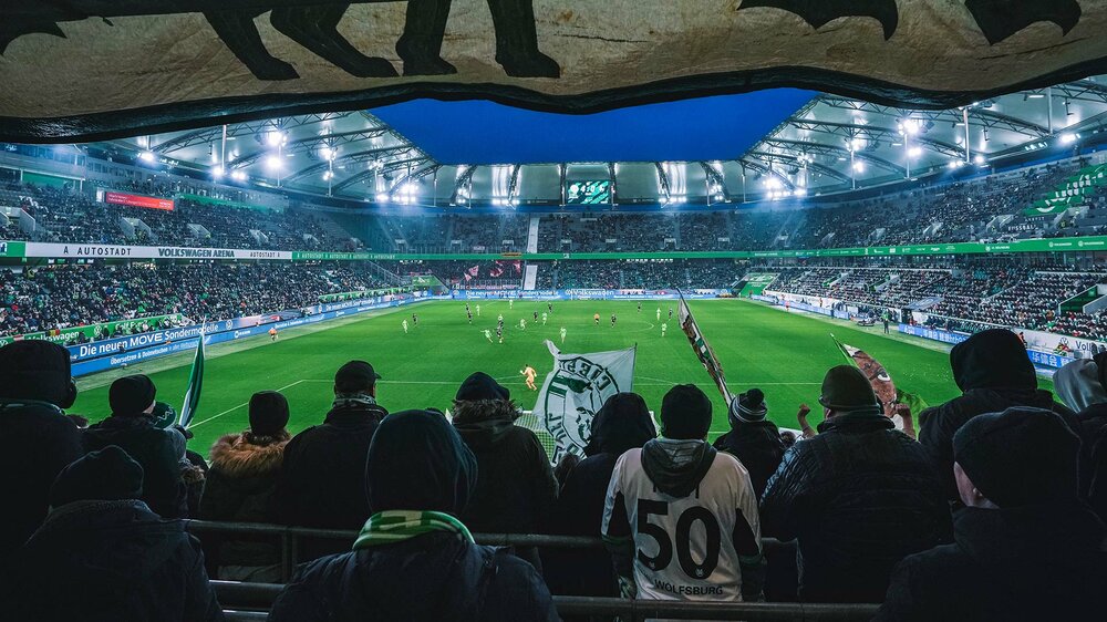 Fans des VfL Wolfsburg stehen in der Nordkurve und schauen aufs Spielfeld.