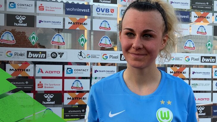 VfL-Wolfsburg-Spielerin Lena Lattwein steht vor einer Sponsorenwand und lächelt.