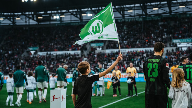 Die Mannschaften laufen ein und ein Junge hält eine VfL Wolfsburg-Fahne hoch.