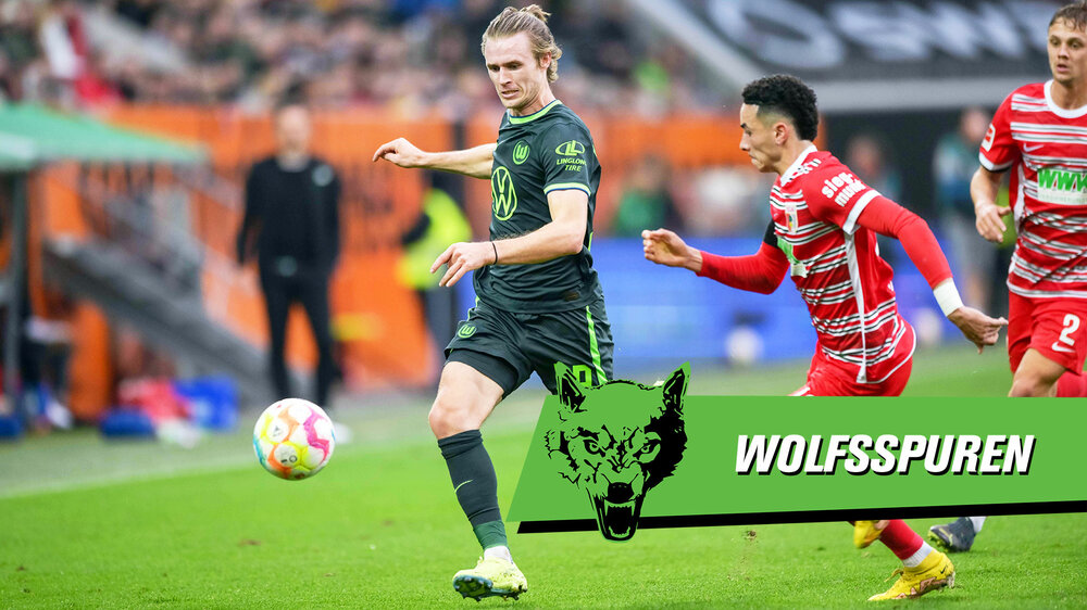 VfL-Wolfsburg-Spieler Patrick Wimmer läuft fokussiert mit dem Ball vor den Gegnern davon, davor befindet sich eine grüne Grafik mit der Aufrschrift "Wolfsspuren".