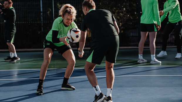 Die VfL-Wolfsburg-Spielerin Lena Lattwein hält lachend einen Ball in der Hand. Ihr gegenüber steht ein Trainer.